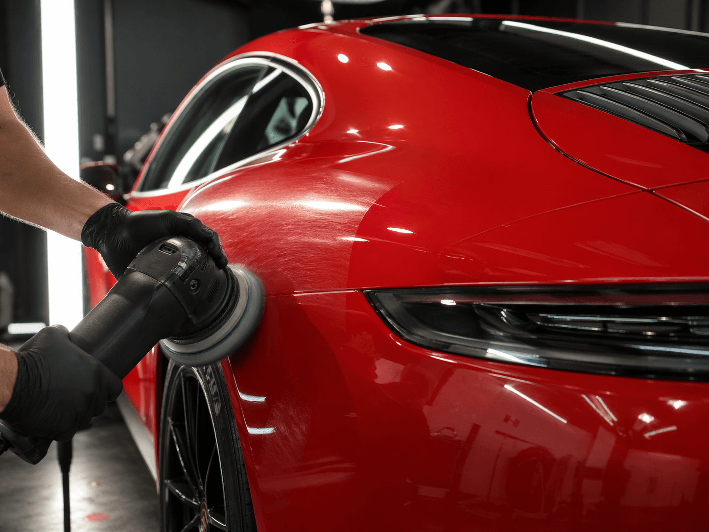 Red Porsche rear quarter being machine polished with a dual-action polisher